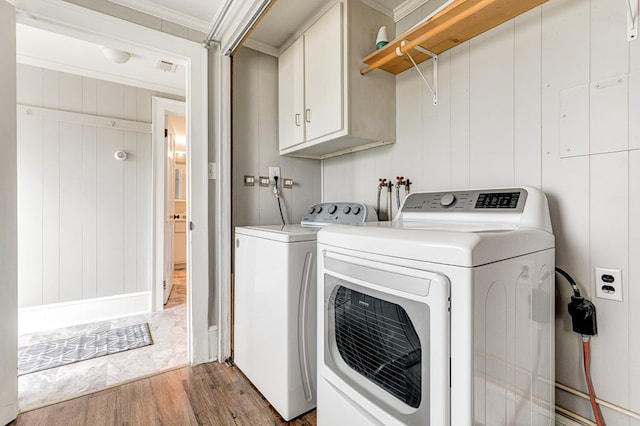 laundry area featuring ornamental molding, cabinet space, washing machine and dryer, and light wood-type flooring