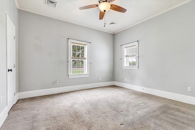 carpeted spare room featuring ornamental molding, ceiling fan, a healthy amount of sunlight, and visible vents