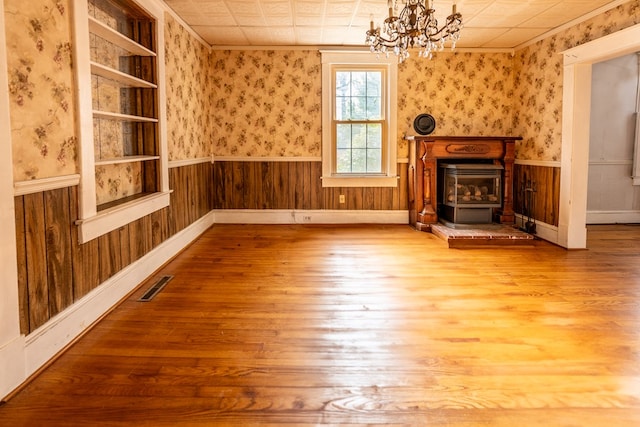 unfurnished living room featuring wood-type flooring, wooden walls, and a notable chandelier