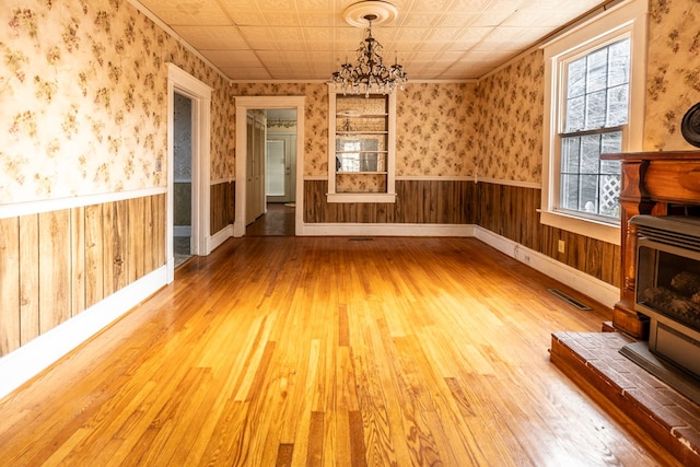 unfurnished living room with hardwood / wood-style floors, a chandelier, and wood walls