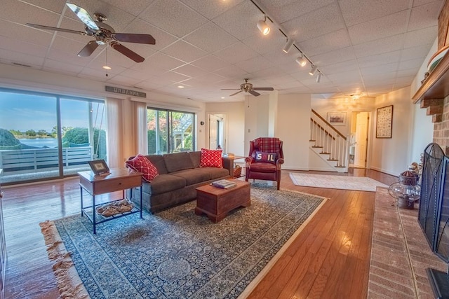 181 Cross St, Urbanna, VA 23175 - living room with track lighting, a ceiling fan, stairs, hardwood / wood-style flooring, and a fireplace