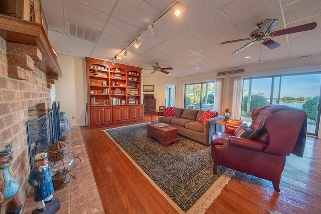 181 Cross St, Urbanna, VA 23175 - living area with a ceiling fan, rail lighting, a brick fireplace, light wood-style floors, and a paneled ceiling