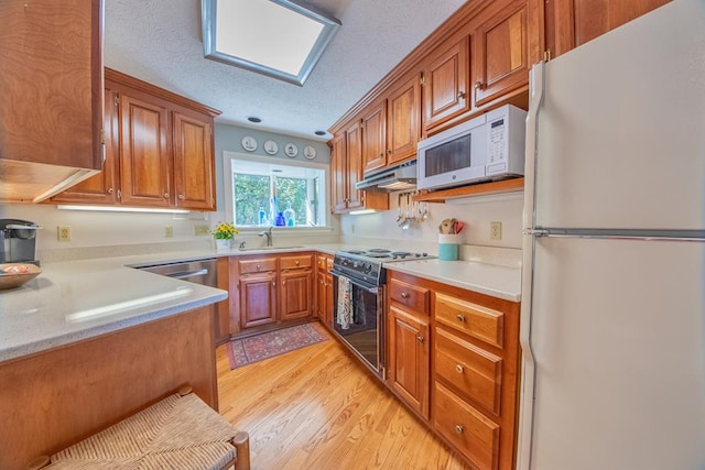 181 Cross St, Urbanna, VA 23175 - kitchen featuring white appliances, under cabinet range hood, brown cabinets, light wood-style flooring, and a textured ceiling
