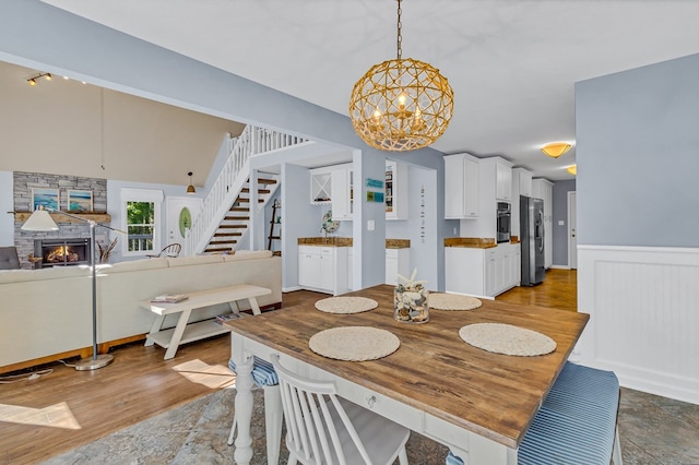 1198 Knights Landing Dr, Heathsville, VA 22473 - dining space with a chandelier, stairway, a stone fireplace, a wainscoted wall, and light stone finish flooring