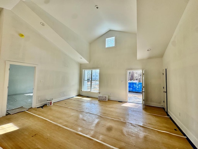 unfurnished living room featuring a healthy amount of sunlight, high vaulted ceiling, and baseboards