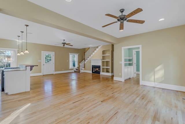 unfurnished living room with built in shelves, ceiling fan, and light hardwood / wood-style flooring