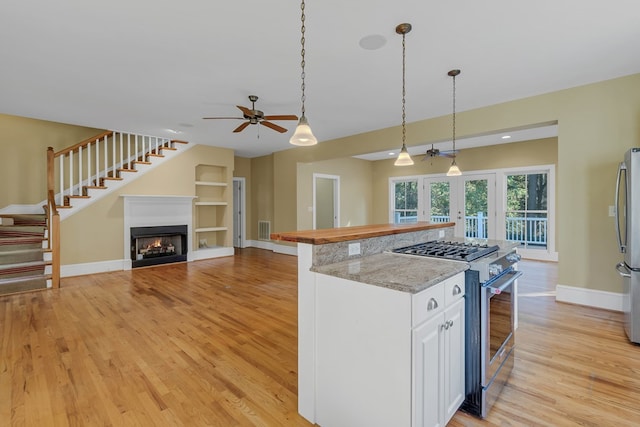 kitchen featuring light hardwood / wood-style flooring, appliances with stainless steel finishes, white cabinetry, light stone counters, and decorative light fixtures