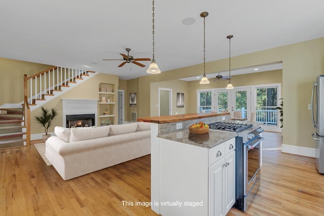 kitchen featuring pendant lighting, stainless steel appliances, light stone countertops, white cabinets, and light wood-type flooring