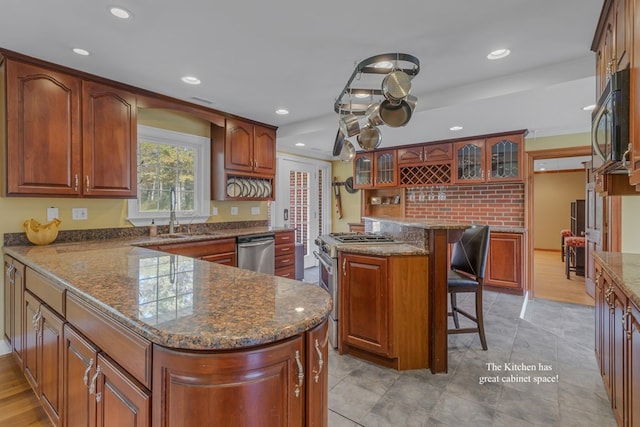 kitchen with a breakfast bar, stone counters, sink, appliances with stainless steel finishes, and a kitchen island