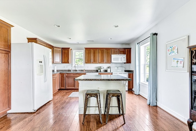 kitchen with a sink, a center island, a kitchen breakfast bar, white appliances, and wood-type flooring