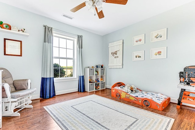 bedroom featuring ceiling fan, visible vents, baseboards, and wood finished floors