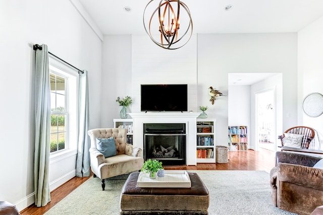 living room with a glass covered fireplace, wood finished floors, recessed lighting, an inviting chandelier, and baseboards