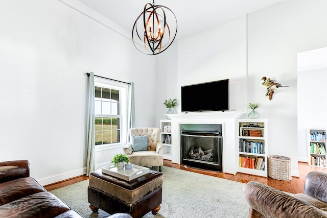 living room with wood finished floors, baseboards, a high ceiling, a fireplace, and a chandelier