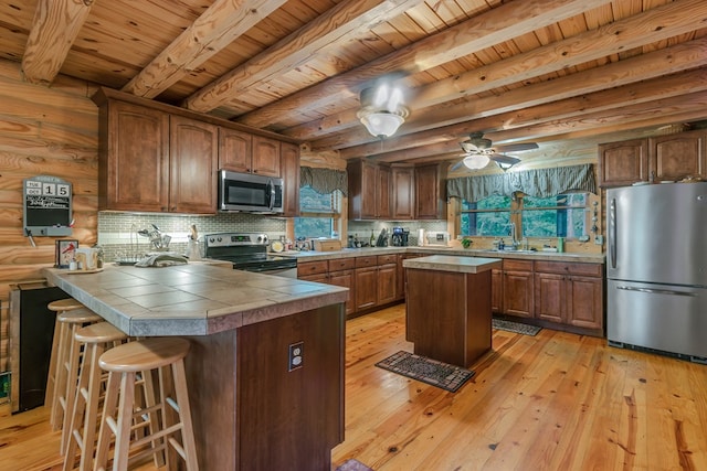 kitchen featuring tile counters, kitchen peninsula, decorative backsplash, appliances with stainless steel finishes, and light wood-type flooring