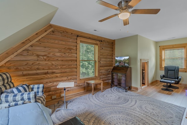 living area featuring ceiling fan, light wood-type flooring, and rustic walls