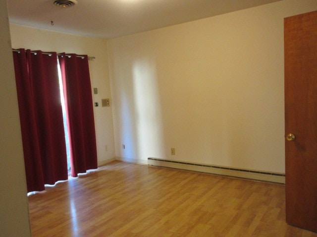 empty room with light hardwood / wood-style flooring and a baseboard heating unit