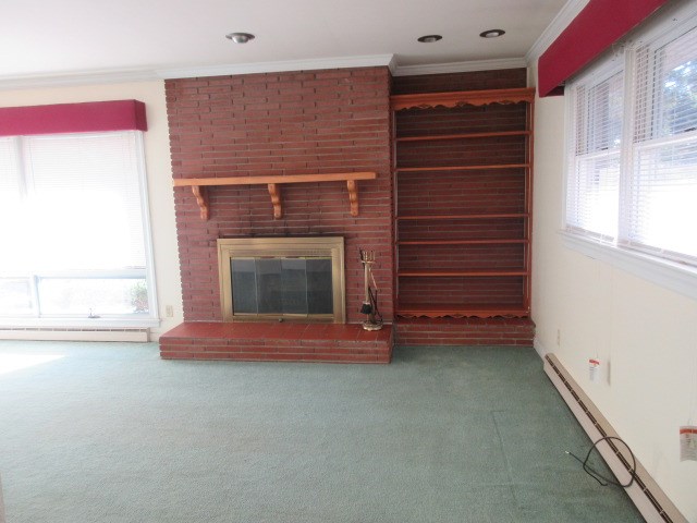 unfurnished living room featuring carpet, crown molding, a fireplace, and a baseboard radiator