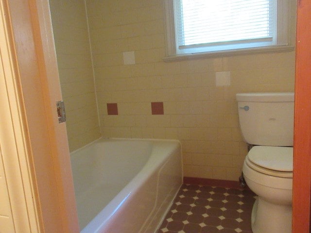 bathroom featuring a bathing tub, tile walls, and toilet