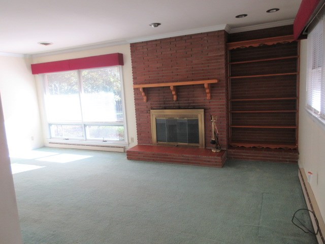 unfurnished living room with a fireplace, ornamental molding, carpet floors, and a healthy amount of sunlight