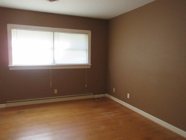 spare room featuring baseboard heating and light hardwood / wood-style flooring