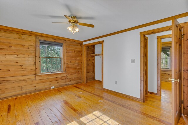 unfurnished bedroom with light wood-style floors, ceiling fan, a closet, wood walls, and baseboards