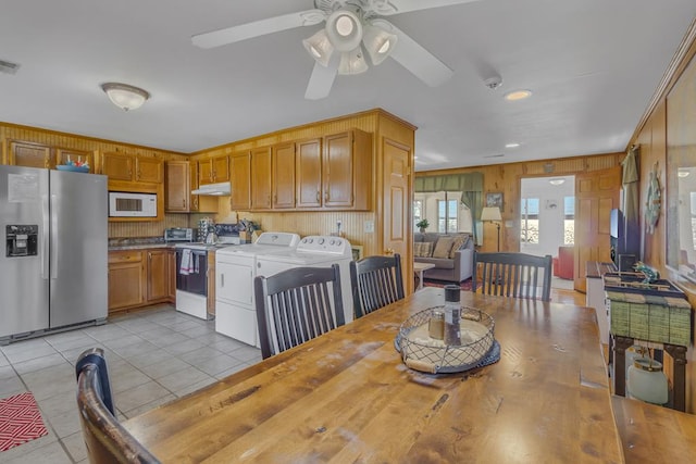 tiled dining area with wood walls, washing machine and clothes dryer, and ceiling fan