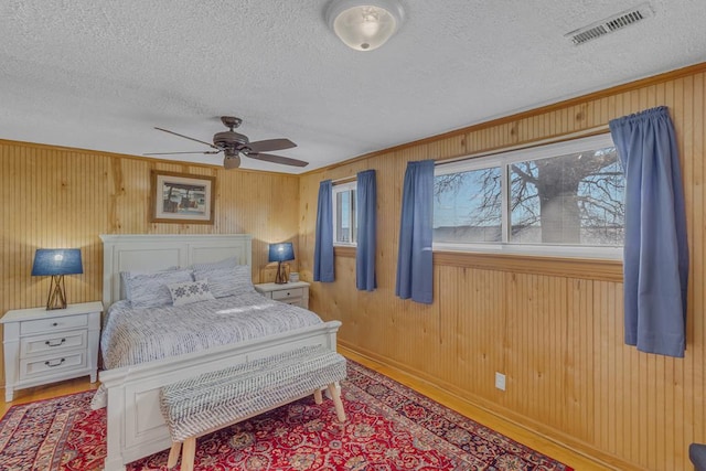 bedroom featuring wood walls, ceiling fan, a textured ceiling, and hardwood / wood-style floors