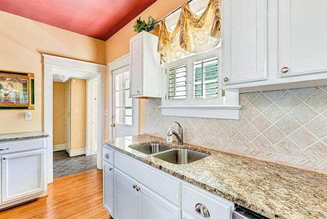 kitchen featuring backsplash, light stone counters, sink, light hardwood / wood-style floors, and white cabinetry