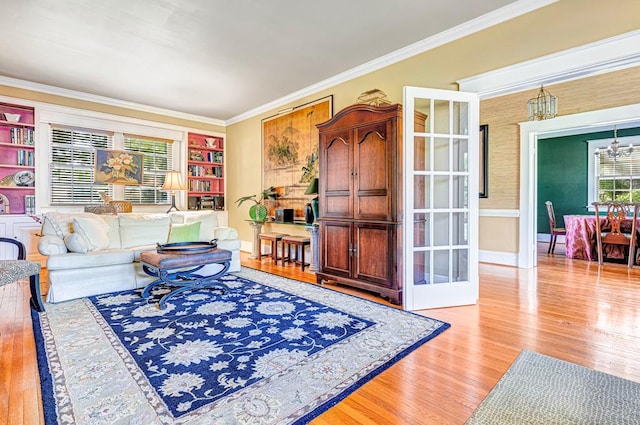 living room with french doors, built in shelves, light wood-type flooring, ornamental molding, and a notable chandelier