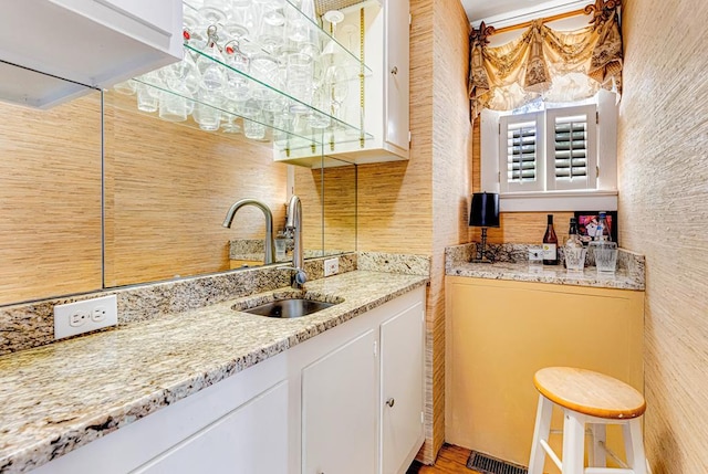 kitchen featuring light stone countertops, white cabinetry, and sink