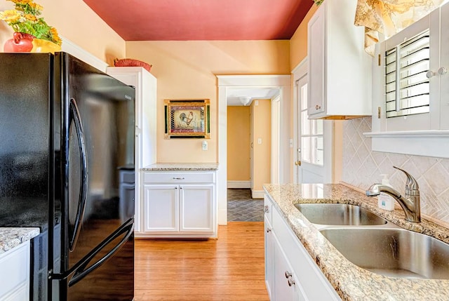 kitchen featuring white cabinets, light stone counters, black fridge, and sink