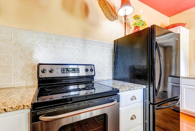 kitchen with white cabinetry, stainless steel electric range oven, light stone countertops, black fridge, and backsplash