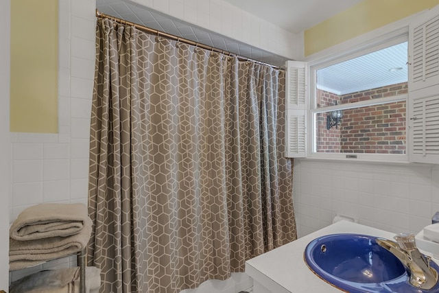 bathroom with curtained shower, a sink, and tile walls