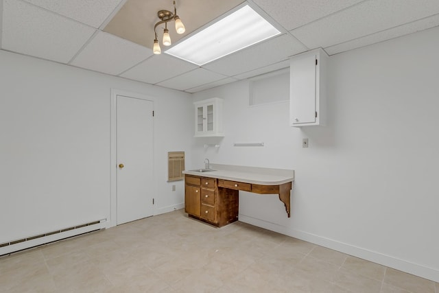 unfurnished office with a sink, a baseboard radiator, a paneled ceiling, and baseboards