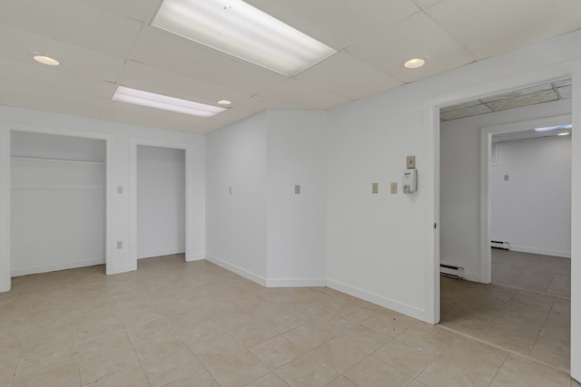 unfurnished room with a paneled ceiling, a baseboard heating unit, and baseboards