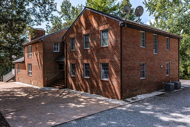 view of home's exterior featuring a chimney, driveway, central AC unit, and brick siding