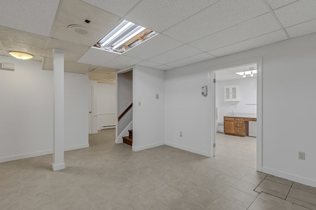 finished basement with stairs, a paneled ceiling, and baseboards