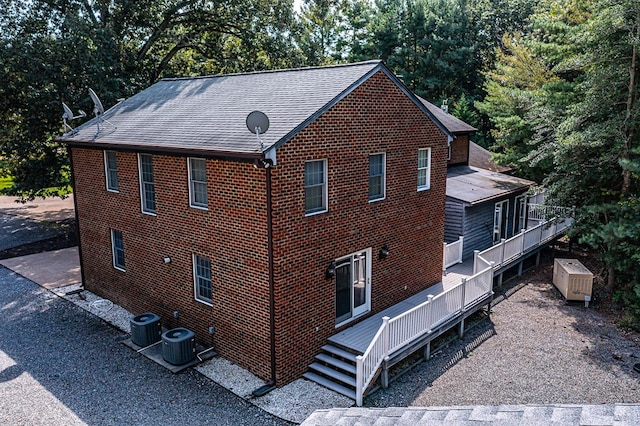 view of side of property featuring central AC unit, a wooden deck, brick siding, and roof with shingles