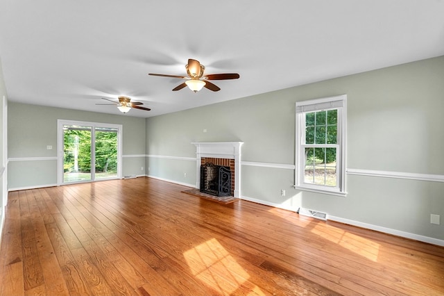 unfurnished living room with hardwood / wood-style flooring, a brick fireplace, and ceiling fan