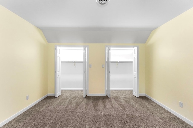 unfurnished bedroom featuring multiple closets, lofted ceiling, and carpet