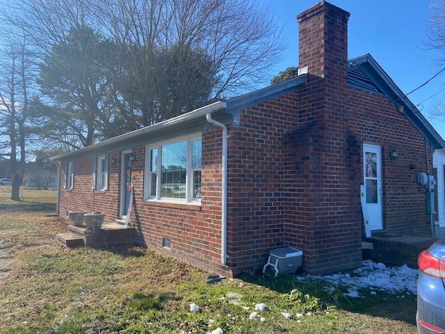 view of property exterior featuring crawl space, brick siding, and a chimney