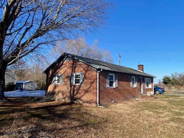 view of home's exterior with brick siding, crawl space, a chimney, and a lawn