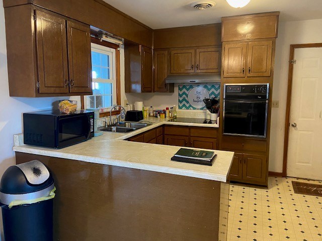 kitchen with under cabinet range hood, a peninsula, a sink, light countertops, and black appliances