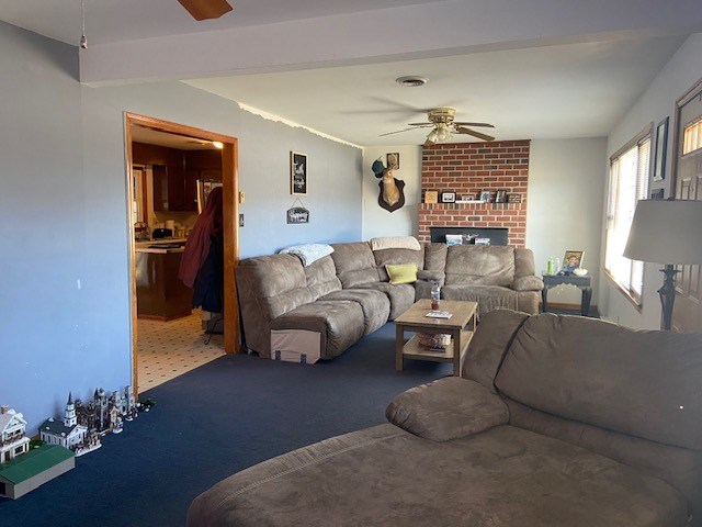 living room with ceiling fan, a brick fireplace, and visible vents