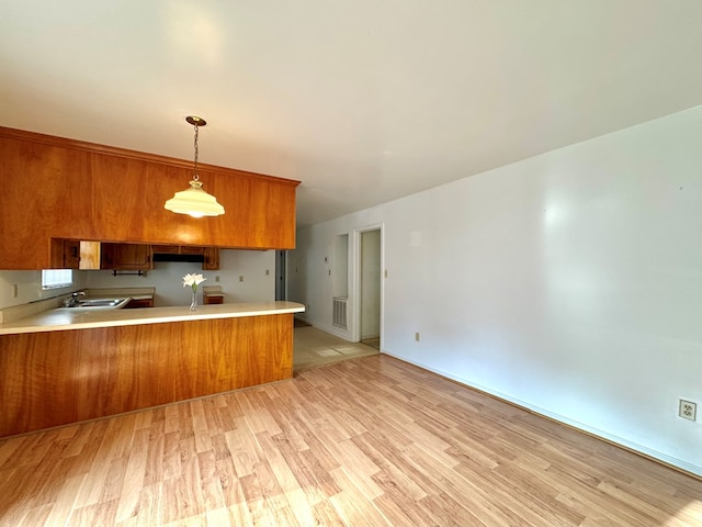 kitchen with decorative light fixtures, light wood-type flooring, kitchen peninsula, and sink