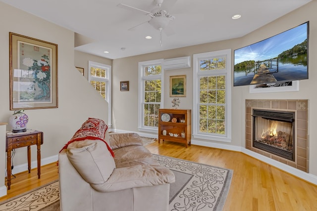 sitting room featuring a wall mounted air conditioner, wood finished floors, ceiling fan, a tile fireplace, and baseboards