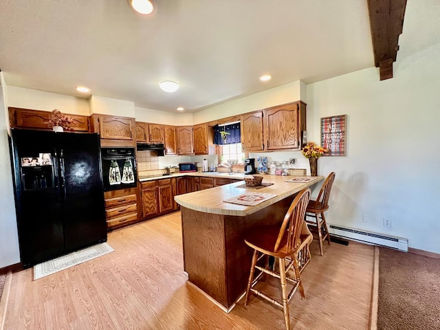 kitchen featuring kitchen peninsula, a kitchen breakfast bar, sink, black appliances, and a baseboard radiator