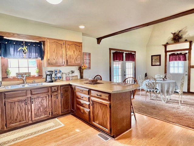 kitchen with kitchen peninsula, light hardwood / wood-style flooring, a healthy amount of sunlight, and sink