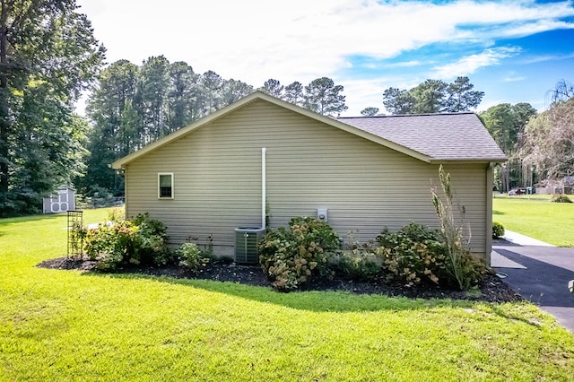 view of side of home with central AC, a yard, and a storage unit