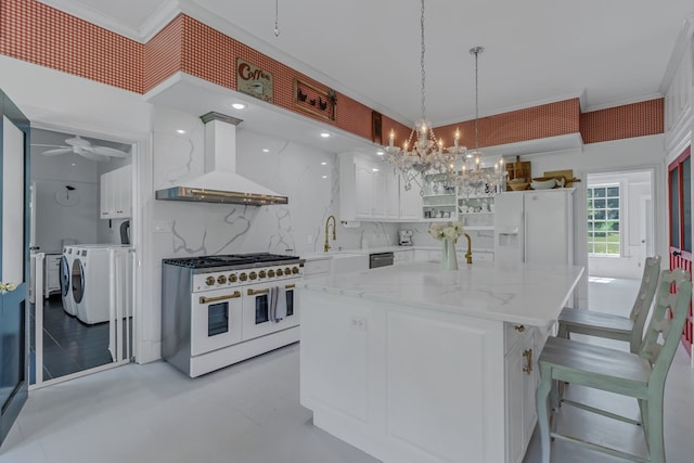 kitchen featuring white appliances, white cabinets, wall chimney range hood, decorative backsplash, and washing machine and clothes dryer